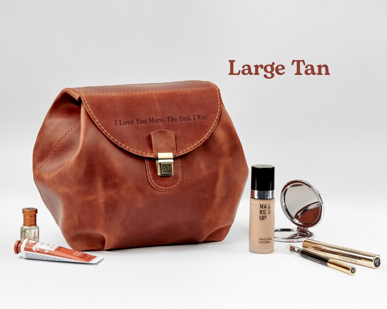 A large tan leather cosmetic bag on table with personaization on the front side. Near cosmetic items. Cosmetic bag for women with monogrammed. Best gift for her.