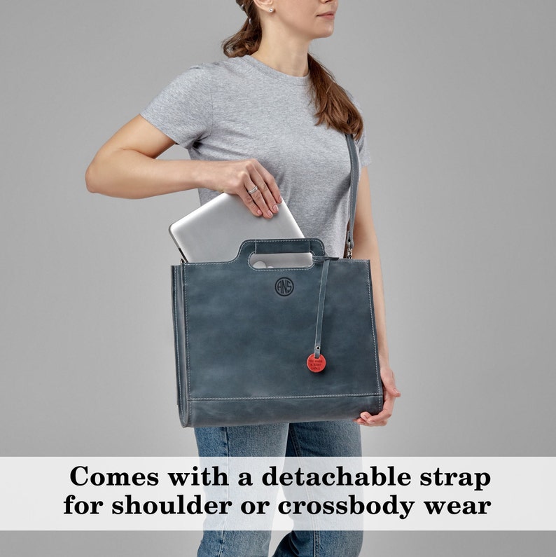 Puede incluir: Un bolso tote de cuero azul oscuro con una correa desmontable. El bolso tiene un asa superior y un peque&ntilde;o bolsillo en la parte delantera. Se puede ver un port&aacute;til dentro del bolso.