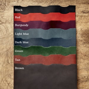 May include: A color swatch of leather samples in various shades, including black, red, burgundy, light blue, dark blue, green, tan, and brown. Each sample is labeled with its corresponding color name. The samples are arranged vertically against a wooden background.