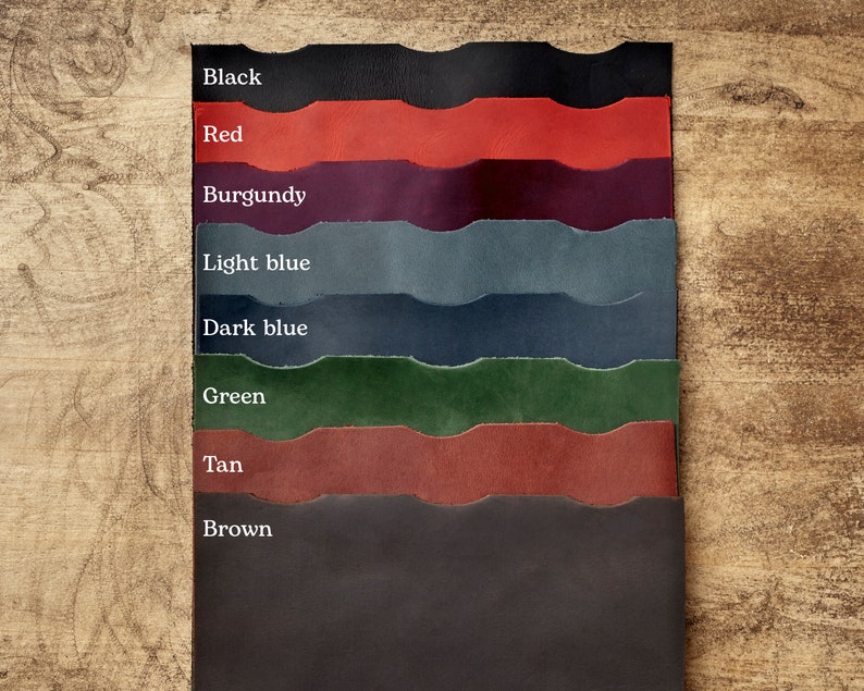 May include: A color swatch of leather samples in various shades, including black, red, burgundy, light blue, dark blue, green, tan, and brown. Each sample is labeled with its corresponding color name. The samples are arranged vertically against a wooden background.