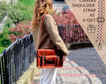 May include: A brown leather satchel with two front pockets and a shoulder strap. The image includes a checkered canvas shoulder strap as a gift. The text in the image reads: "ADDITIONAL CANVAS SHOULDER STRAP AS A GIFT."