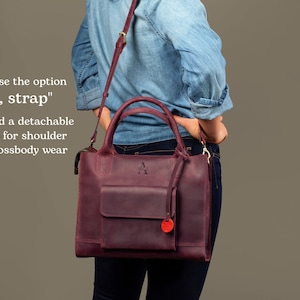 May include: A burgundy leather handbag with a detachable shoulder strap. The bag has a front pocket and a gold metal zipper. The bag has a gold metal handle and a gold metal letter "A" embossed on the front.
