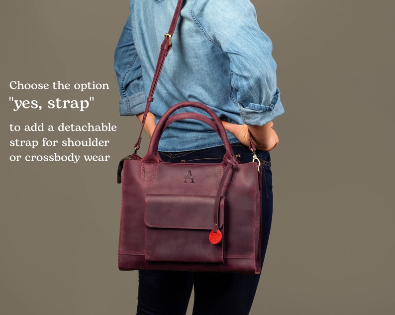 May include: A burgundy leather handbag with a detachable shoulder strap. The bag has a front pocket and a gold metal zipper. The bag has a gold metal handle and a gold metal letter "A" embossed on the front.