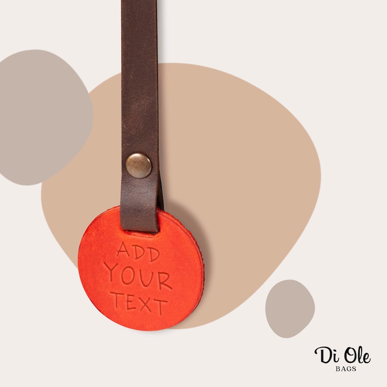 May include: A red leather keychain with a brown leather strap. The keychain has the text "ADD YOUR TEXT" embossed on it.