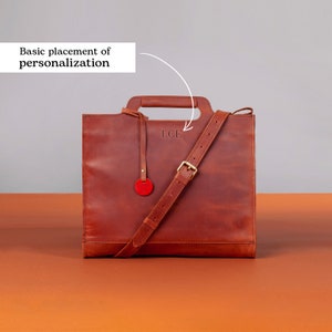 Puede incluir: Un bolso tote de cuero marr&oacute;n con asa superior y una correa larga ajustable. El bolso tiene una inscripci&oacute;n personalizada que dice "L.C.F."