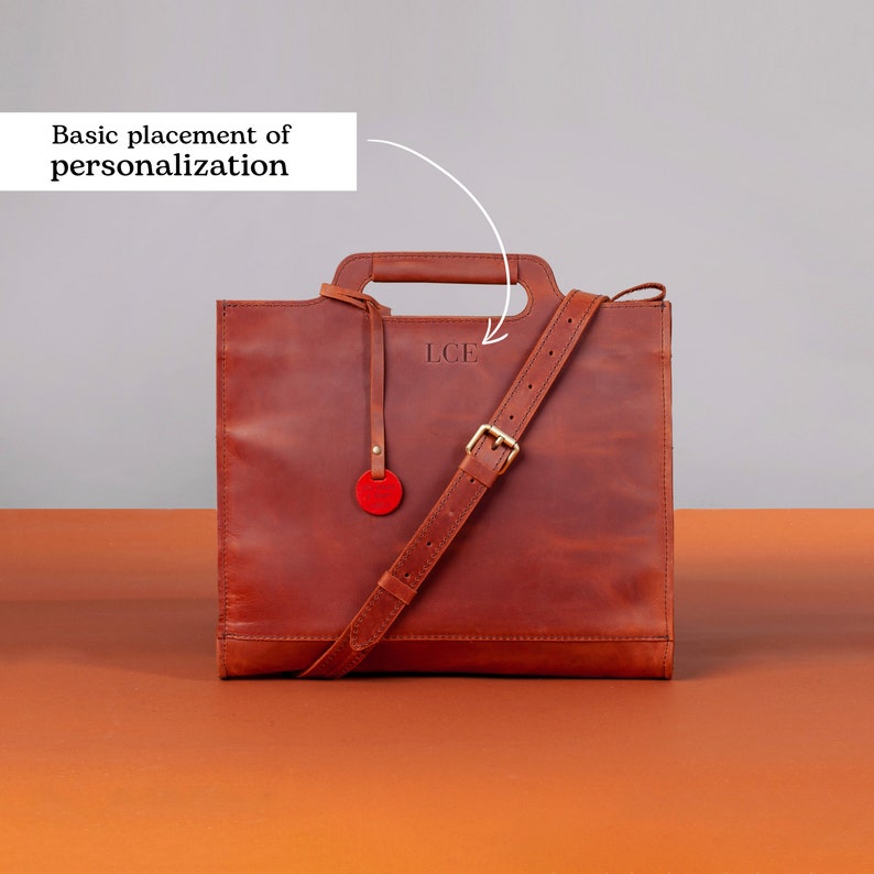 Puede incluir: Un bolso tote de cuero marr&oacute;n con asa superior y una correa larga ajustable. El bolso tiene una inscripci&oacute;n personalizada que dice "L.C.F."