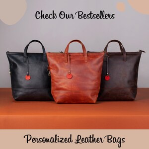 May include: Three leather tote bags in black, brown, and orange. The bags have a zipper closure and a small red circle on the front. The text "Check Our Bestsellers" is at the top of the image and "Personalized Leather Bags" is at the bottom.
