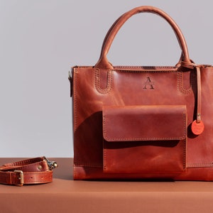 May include: A brown leather tote bag with a front pocket and a detachable shoulder strap. The bag has a logo that says "Arlo & Co."