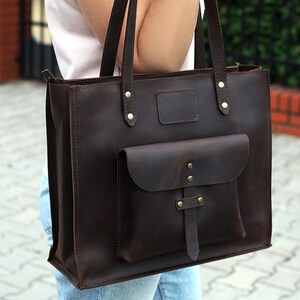 May include: A brown leather tote bag with a zipper closure and a front pocket. The bag has a strap and a handle.