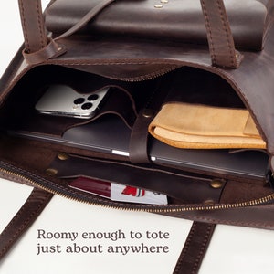 May include: A brown leather tote bag with a zipper closure, interior pockets, and handles. The bag contains a laptop, a smartphone, and a leather case. The text "Roomy enough to tote just about anywhere" is visible.
