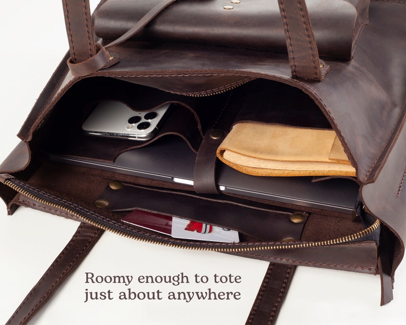 May include: A brown leather tote bag with a zipper closure, interior pockets, and handles. The bag contains a laptop, a smartphone, and a leather case. The text "Roomy enough to tote just about anywhere" is visible.