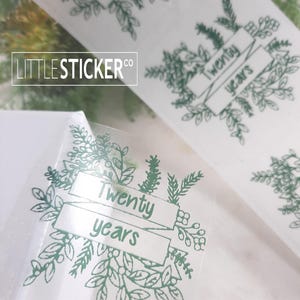 May include: Green foliage sticker with a banner that reads "Twenty years".