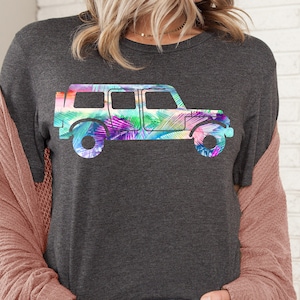 May include: A dark grey t-shirt with a colorful graphic of a jeep silhouette. The jeep is filled with a watercolor-like design of tropical leaves in shades of pink, blue, green, and purple.