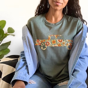 May include: A teal green sweatshirt with a floral print pickup truck design. The truck is outlined in brown and the flowers are in shades of red, orange, yellow, and green.