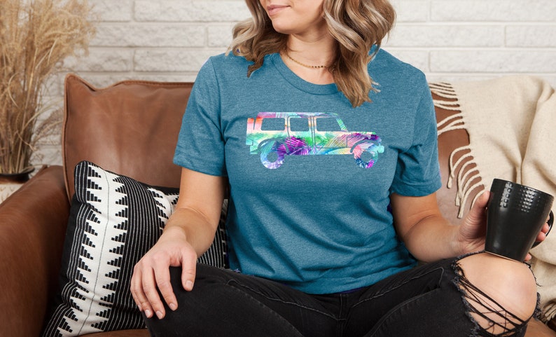 May include: A teal blue t-shirt with a colorful floral print of a jeep silhouette.