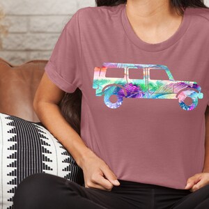 May include: A mauve t-shirt with a colorful graphic of a jeep silhouette. The jeep is filled with a tropical leaf pattern in shades of pink, purple, green, and blue.