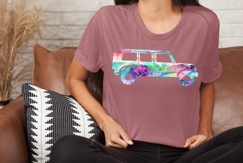 May include: A mauve t-shirt with a colorful graphic of a jeep silhouette. The jeep is filled with a tropical leaf pattern in shades of pink, purple, green, and blue.