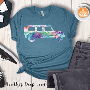 May include: A teal blue t-shirt with a floral print of a jeep silhouette. The text "Heather Deep Teal" is printed on the bottom of the shirt.