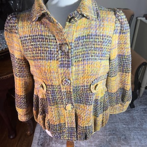 May include: A yellow, brown, and purple plaid jacket with a button-up front and long sleeves. The jacket has a slightly puffed-out style.