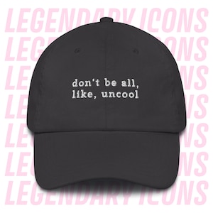 Könnte beinhalten: Dunkelgraue Baseballkappe mit dem gestickten Text "don't be all, like, uncool" in Weiß. Die Kappe hat einen gebogenen Schirm und einen Knopf oben. Der Hintergrund zeigt die Worte "LEGENDARY ICONS" in Rosa.
