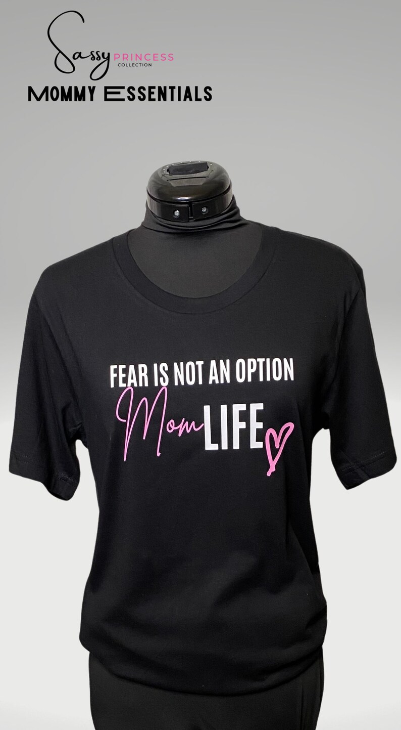 May include: Black t-shirt with white text that reads "Fear is not an option Mom Life" with a pink heart. The text "Mom Life" is in a pink script font.