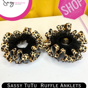 May include: Two black elastic hair ties with leopard print ruffle trim. The hair ties are on a white surface. SASSY TUTU RUFFLE ANKLETS www.sassyprincesscollection.com