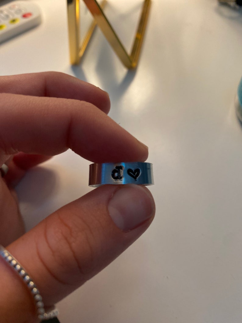 May include: A silver ring with a black heart and the letter "d" engraved on it.