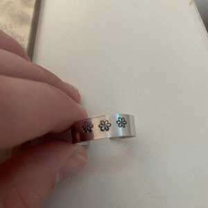 May include: A silver metal ring with three small flower designs engraved on the band.