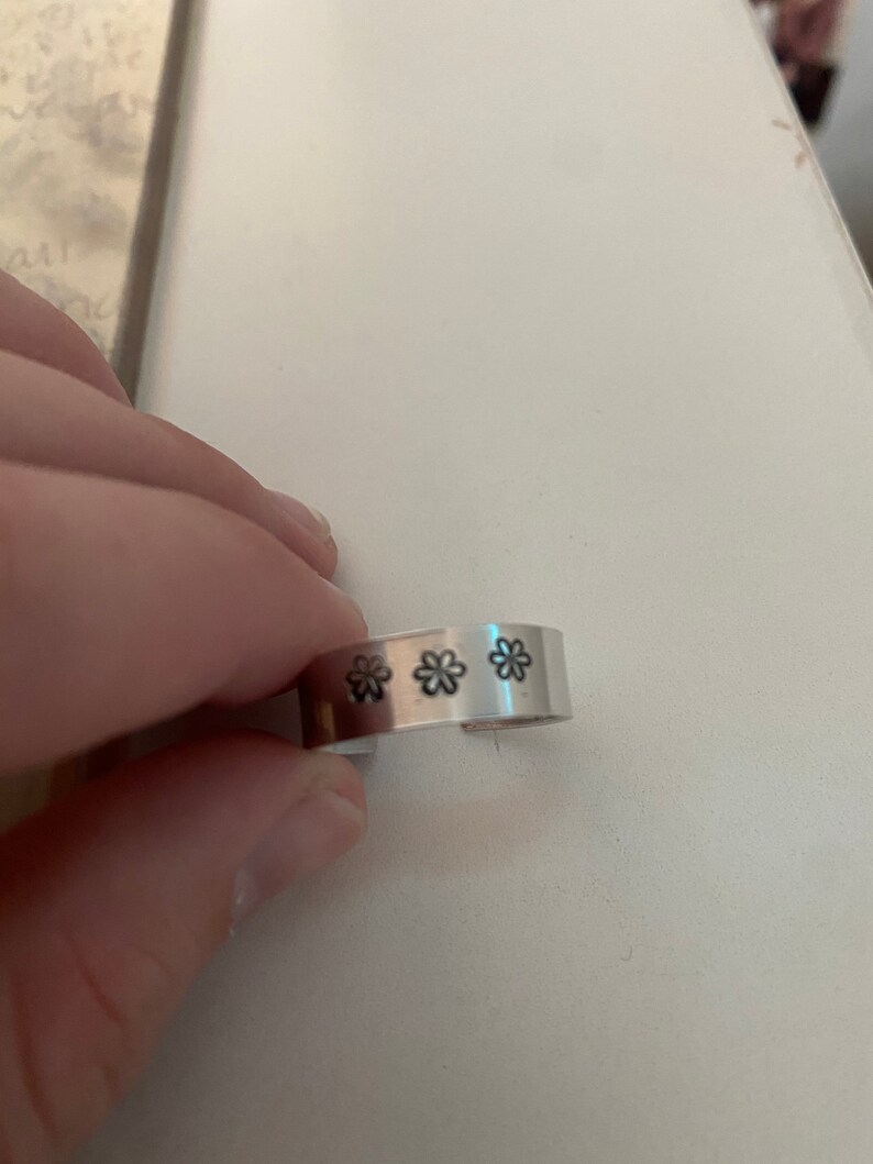 May include: A silver metal ring with three small flower designs engraved on the band.