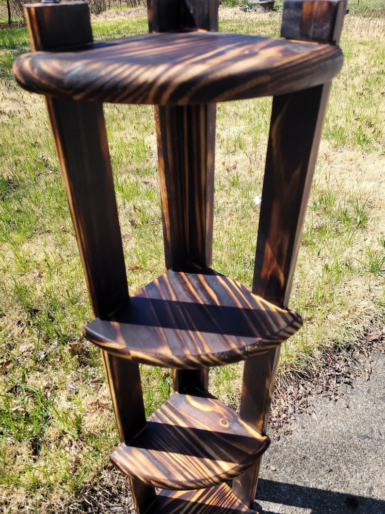 Puede incluir: Una estanter&iacute;a de esquina de madera con cuatro niveles. Las estanter&iacute;as son de madera oscura con un acabado quemado. La estanter&iacute;a es independiente y tiene un aspecto r&uacute;stico.