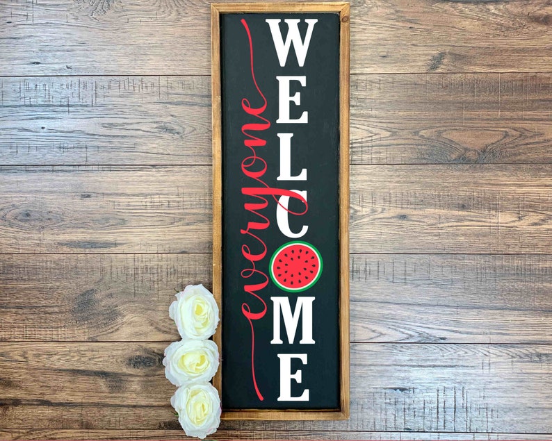 Puede incluir: Un letrero de madera negro con letras blancas que dice "Bienvenido a todos" con un gr&aacute;fico de sand&iacute;a roja en el centro.