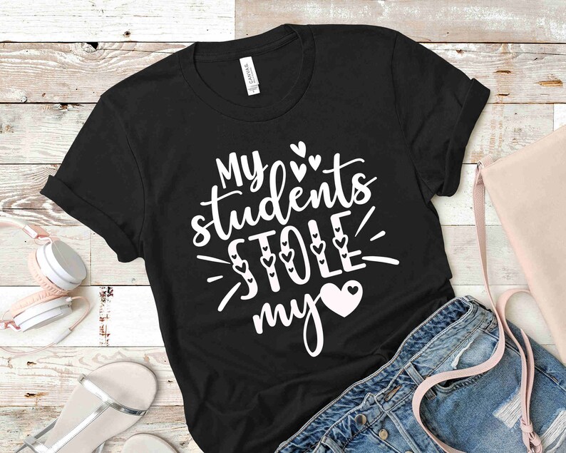 Może przedstawiać: Czarny T-shirt z białym tekstem, kt&oacute;ry brzmi "Moi uczniowie ukradli mi serce" z małymi sercami wok&oacute;ł tekstu.