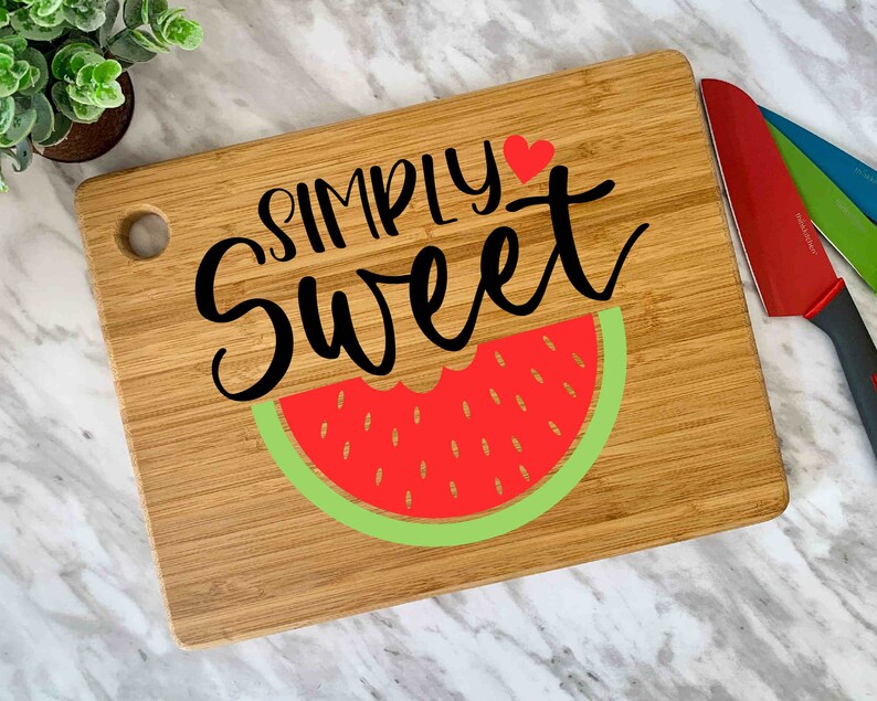 Puede incluir: Una tabla de cortar de madera con un dise&ntilde;o de sand&iacute;a y el texto "SIMPLY Sweet" con un coraz&oacute;n rojo.