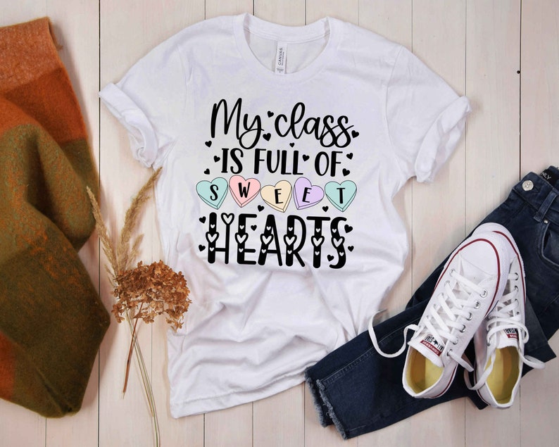 Może przedstawiać: Biała koszulka z napisem "My class is full of sweet hearts" czarnymi literami. Tekst jest otoczony małymi r&oacute;żowymi, niebieskimi i zielonymi sercami.