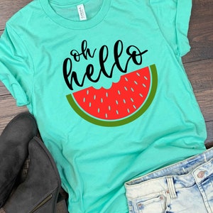 Puede incluir: Una camiseta turquesa con el texto "oh hello" en letra negra y un gr&aacute;fico de rodaja de sand&iacute;a roja.