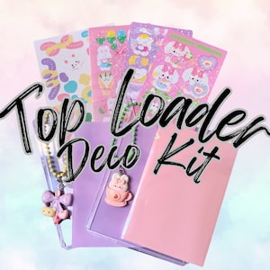 Puede incluir: Un archivador de carga superior rosa y morado con una cubierta frontal transparente. El archivador está decorado con una cadena verde y amarilla con un dije adjunto. El dije es un conejito rosa sosteniendo una taza. El archivador está rodeado de hojas de pegatinas con un tema de conejito rosa y blanco. El texto "Top Loader Deco Kit" está escrito en negro sobre un fondo blanco.