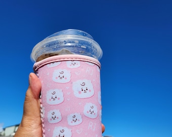 May include: Pink insulated cup sleeve with a cartoon character pattern. The sleeve features a white bear with a pink nose and a pink heart. The text "RJ" is visible on the sleeve.