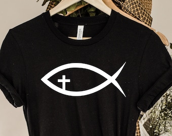 May include: Black t-shirt with a white fish symbol with a cross inside. The fish symbol is a Christian symbol.
