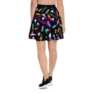 May include: A black skater skirt with a colorful geometric pattern. The skirt features a variety of shapes and colors, including pink, blue, green, yellow, and orange. The skirt is made of a soft, comfortable fabric and is perfect for a casual or dressy occasion.