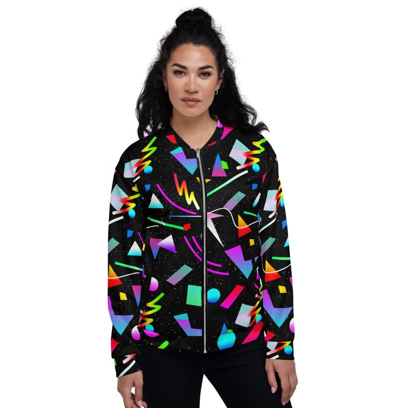 Op de afbeelding: Een zwarte bomberjack met een kleurrijk geometrisch patroon. Het patroon omvat verschillende vormen, lijnen en kleuren, waaronder roze, blauw, groen, geel en oranje. De jas heeft een ritssluiting en een geribbelde kraag, manchetten en zoom.