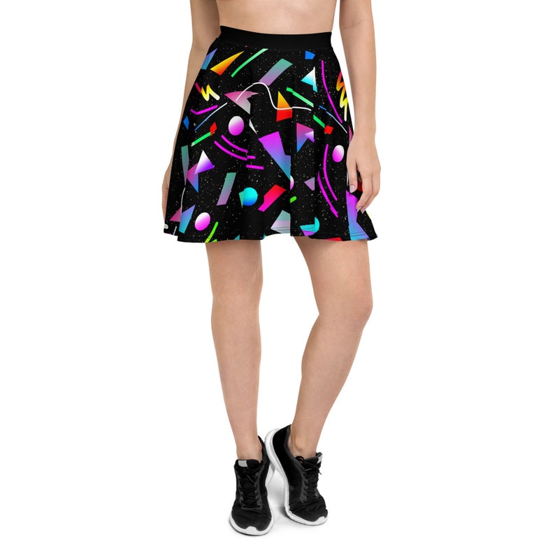 May include: A black skater skirt with a colorful geometric pattern. The pattern includes various shapes and colors, such as triangles, circles, and lines in shades of pink, blue, green, and yellow. The skirt is worn by a person with bare legs and black sneakers.
