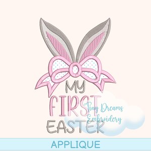 Könnte beinhalten: Rosa und graue gestickte Applikation mit Hasenohren und Schleife. Der Text "My First Easter" befindet sich unter der Schleife.