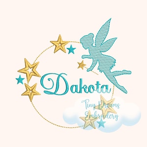 Puede incluir: Diseño bordado con un hada azul volando con una varita mágica, rodeada de estrellas doradas y un círculo con el nombre Dakota. El diseño también incluye una nube con el texto "Tiny Dreams Embroidery".