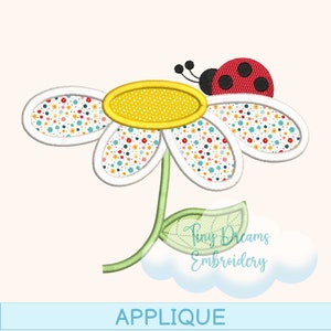 May include: Applique embroidery design featuring a white daisy with a yellow center and a red ladybug on top. The daisy has a green stem and a leaf. The design is labeled "Tiny Dreams Embroidery" and "Applique".