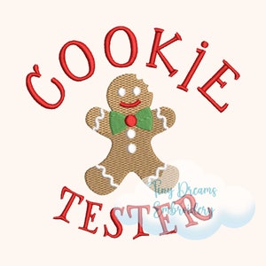 Puede incluir: Texto bordado en rojo "COOKIE TESTER" con un hombre de jengibre en el centro. El hombre de jengibre es marrón con glaseado blanco y una corbata de lazo verde.