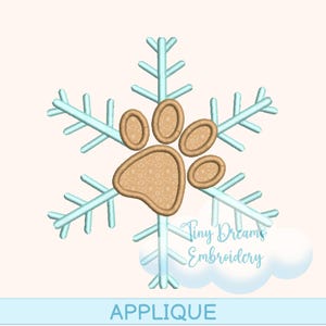 Peut inclure: Un motif de flocon de neige bleu clair avec une empreinte de patte beige au centre. Le mot "APPLIQUE" est écrit en bleu en bas de l'image. Les mots "Tiny Dreams Embroidery" sont écrits en police script sur le côté droit de l'image.
