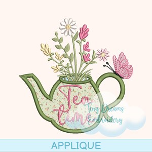 Può includere: Un design di applicazione con una teiera verde piena di fiori colorati e la scritta "Tea Time" in rosa. Una farfalla rosa è posata sul manico. La parola "APPLIQUE" è in basso.