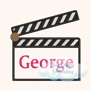 May include: A black and white striped clapperboard with a brown knob. The word "George" is written in pink letters on the clapperboard.