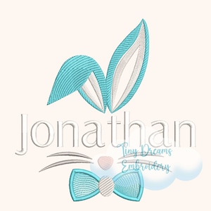 May include: An embroidered design of a bunny with blue ears, a bow tie, and whiskers. The name "Jonathan" is embroidered above the bunny. The text "Tiny Dreams Embroidery" is embroidered below the bunny.
