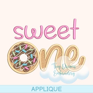 May include: An applique design featuring the words "sweet one" in pink and tan. The "one" is designed as a donut with chocolate frosting and sprinkles. The word "applique" is at the bottom.